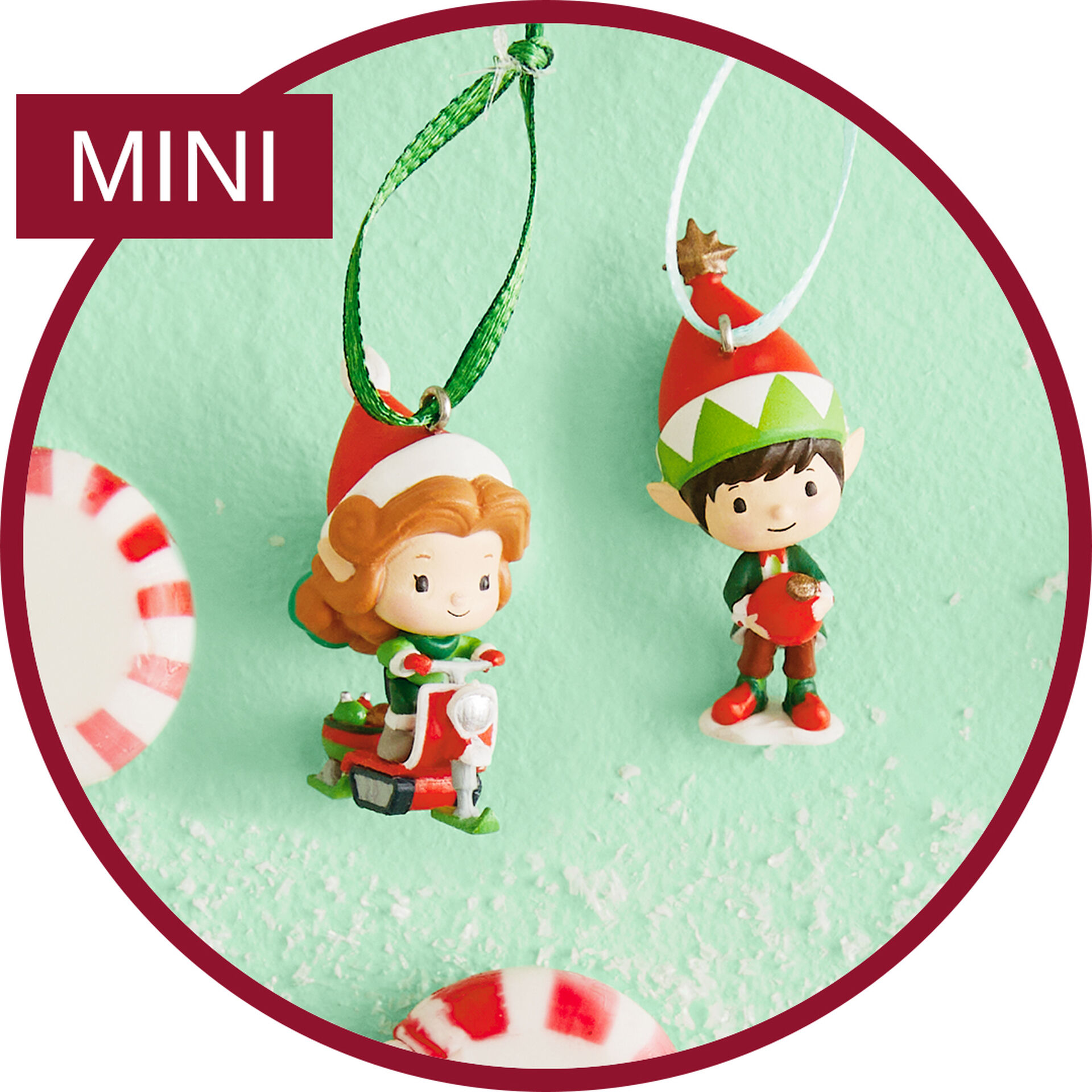 two miniature ornaments of elves next to peppermints on a mint green background