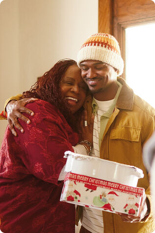 Man hugging an older woman and holding a gift and tupperware.