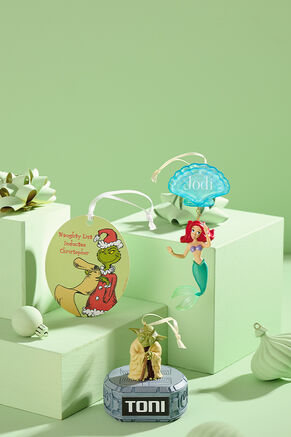 Grinch, Little Mermaid and Yoda ornaments with personalized names on green boxes with bows.