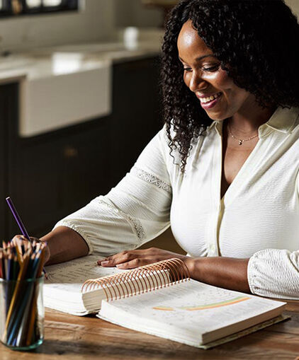 Woman smiling at desk writing in a spiral notebook