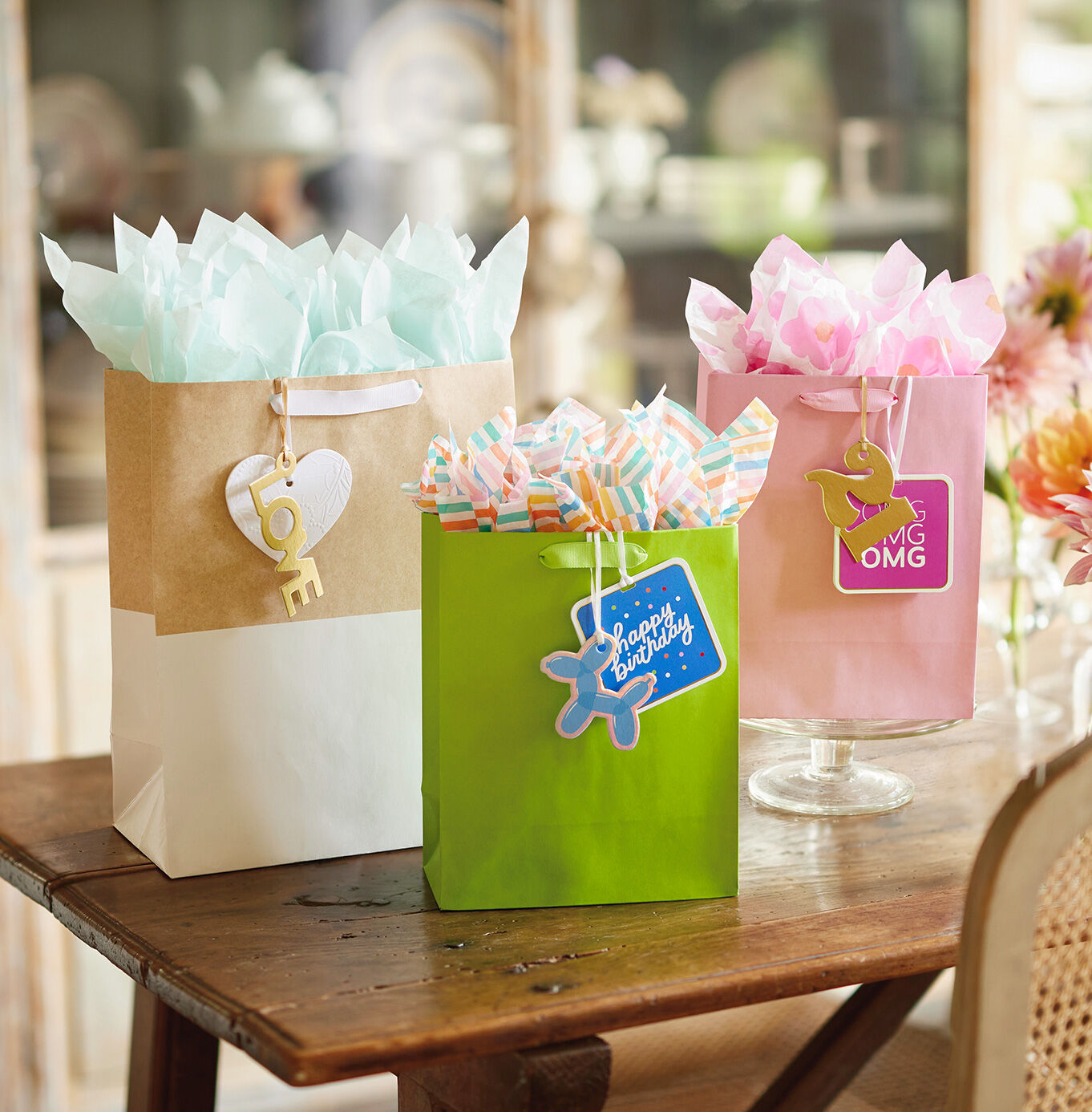 Gold and wite, green, and pink gift bags with matching gift tags on a table. 