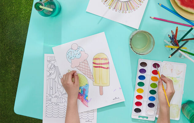 Pair of hands using watercolor to paint summer-themed coloring pages