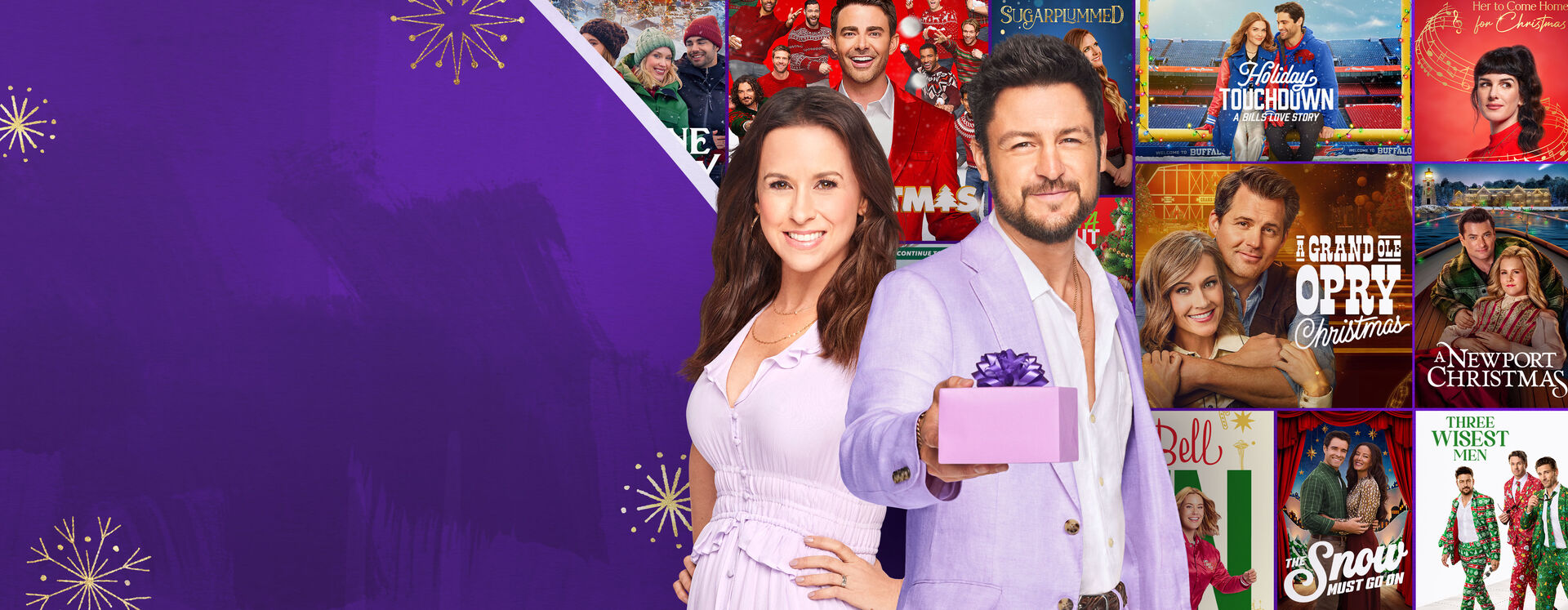 Lacey Chabert and Tyler Hines standing in front of Hallmark holiday movie posters