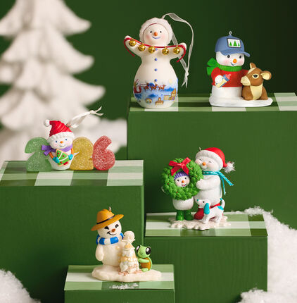Five snowman-themed ornaments on green stands.
