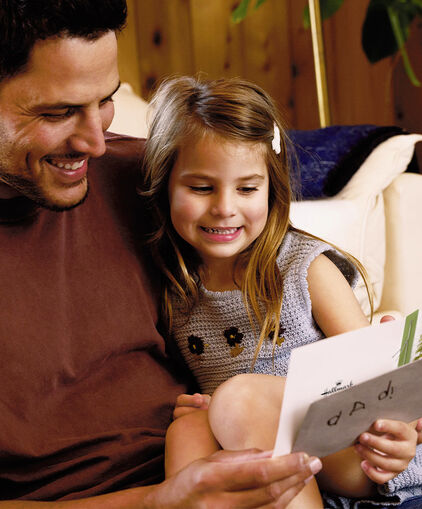 Father and daughter sitting on couch together and smiling at a greeting card