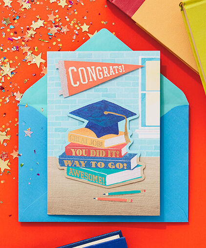 Graduation card on a blue envelope and surrounded by books. 