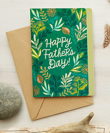 Green Happy Fathers Day card with decorative leaves and greenery on a table.