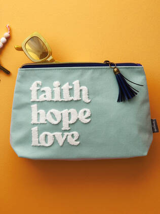 Mint green pouch with faith hope love' on it with zipper tassel on tangerine background.