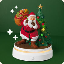Santa standing beside a Christmas tree with a sack of gifts over his shoulder