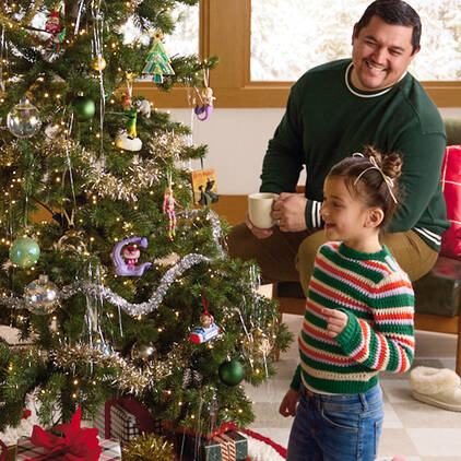 A smiling girl and her father next to a Christmas tree