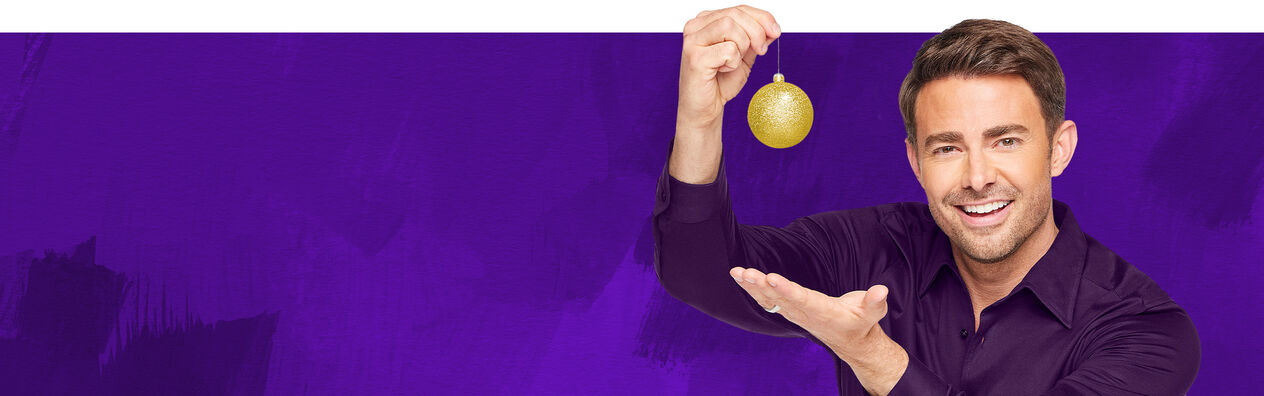 Brunet man holding up a golden, glittery orb ornament and smiling