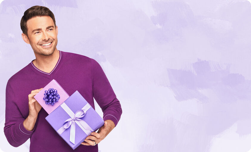 Brown haired man in purple holding two gift wrapped presents.
