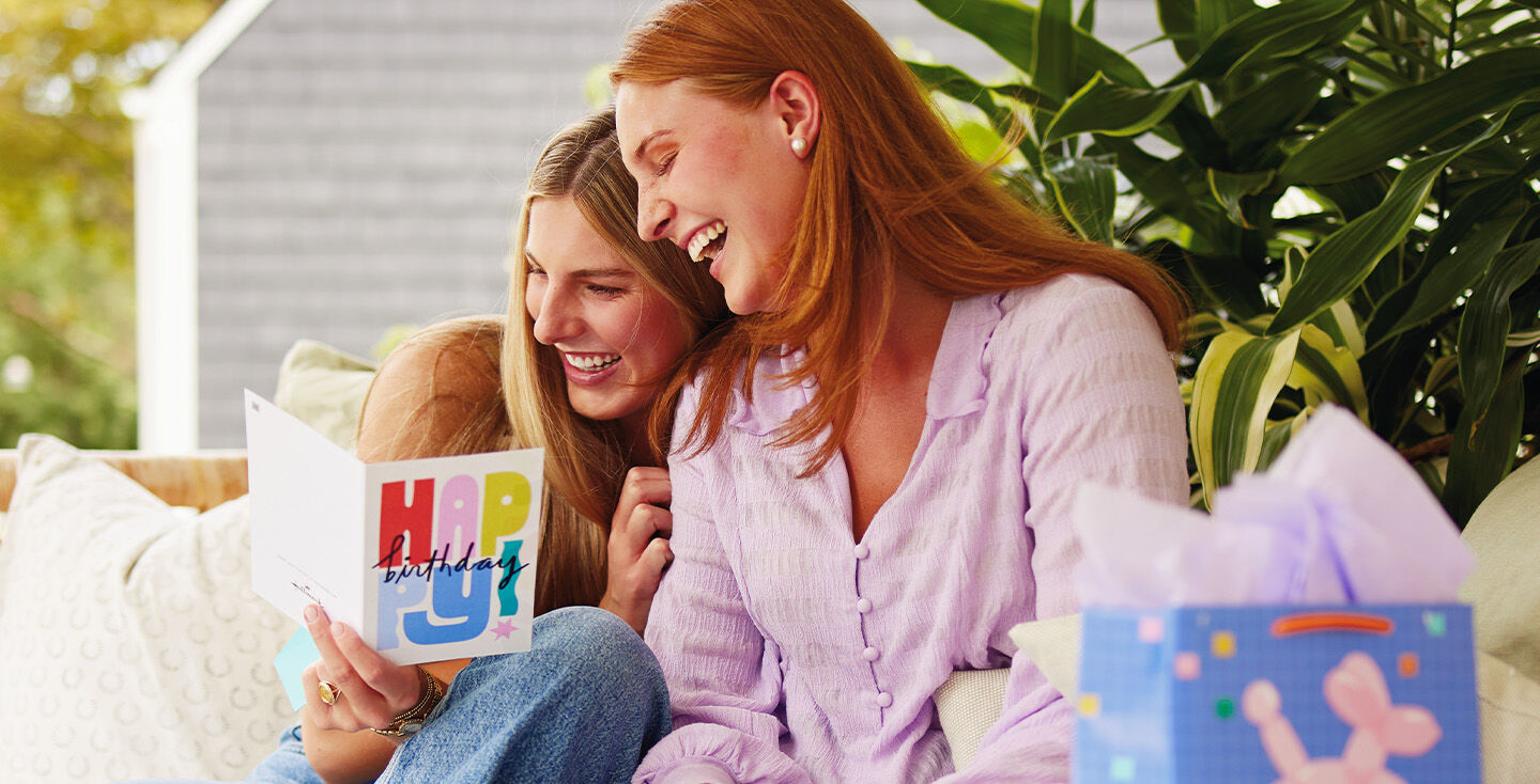 Two women leaning together and laughing as they read a birthday card together.