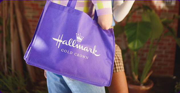Woman holding a purple shopping bag with Hallmark Gold Crown in white on the side