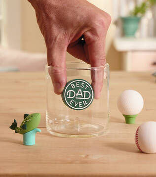 A hand putting a Best Dad Ever' charm into a glass.