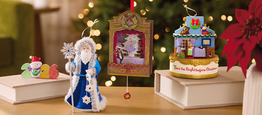 Four holiday-themed ornaments sitting on a table with books and poinsettias. 