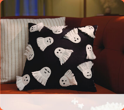 Black pillow with white ghosts on a sofa.
