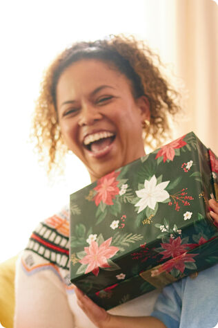 Woman laughing while she holds a gift wrapped in Christmas-themed wrapping paper. 