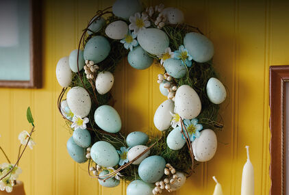 Speckled white and blue eggs on wreath with blue and white flowers, wisps of green grass, and clusters of faux white berries