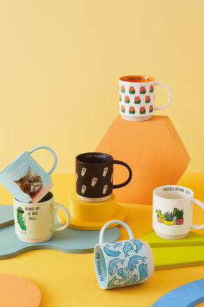 Mugs featuring cats, plants, dolphins, dumpter fires and a pickle displayed on an orange background