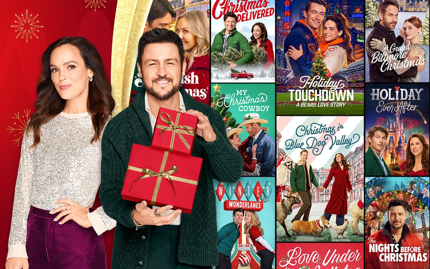 Hallmark stars Erin Cahill and Tyler Hynes in front of a collage of Hallmark Channel Christmas movie posters
