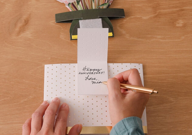 Woman writing on a happy anniversary card attached to a paper vase