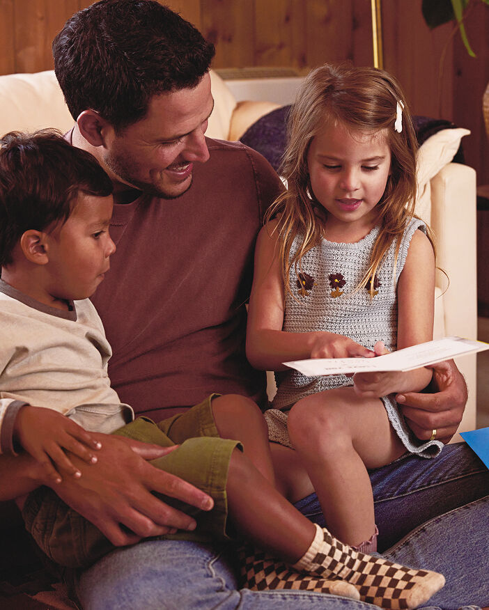Father holding a daughter and son as they look at a Fathers Day card