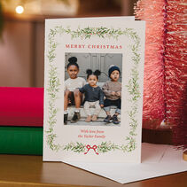 Flat card with your photo bordered by illustrated green garland, berries and a red bow red lettering