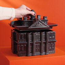 Hand lifting the lid of black Haunted Mansion shaped treat jar. 