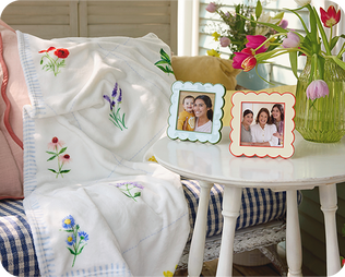 White floral blanket on a sofa with enamel frames on a side table.