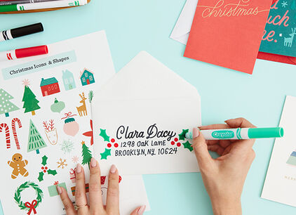 Hands decorating an envelope and surrounded by decorating tools. 