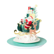 Musical pop-up Christmas greeting card with die-cut Santa Claus, penguin and reindeer in a jade green sleigh filled with gifts and a Christmas tree with foil accents with laser-cut details.