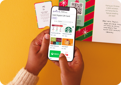 Hands holding a phone and adding a digital gift card to a paper card.
