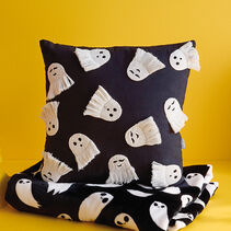 Square, black pillow embroidered with white ghosts sitting on folded black fleece blanket with white ghosts