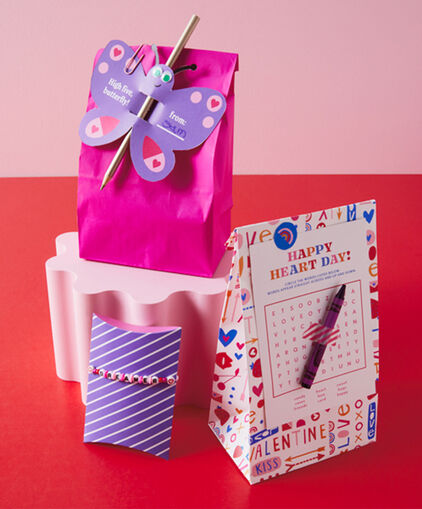 3 Valentines Day DIY treat bags sit on red surface.