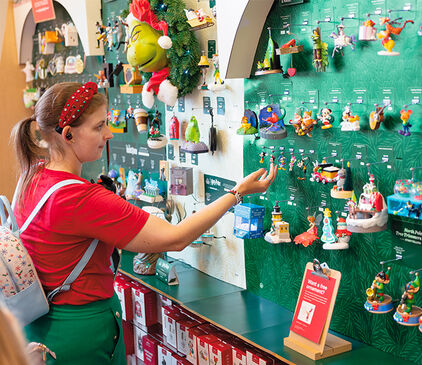 Woman standing in front of a Keepsake Ornament wall in store.
