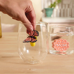 a hand placing a butterfly charmer figurine into a drinking glass