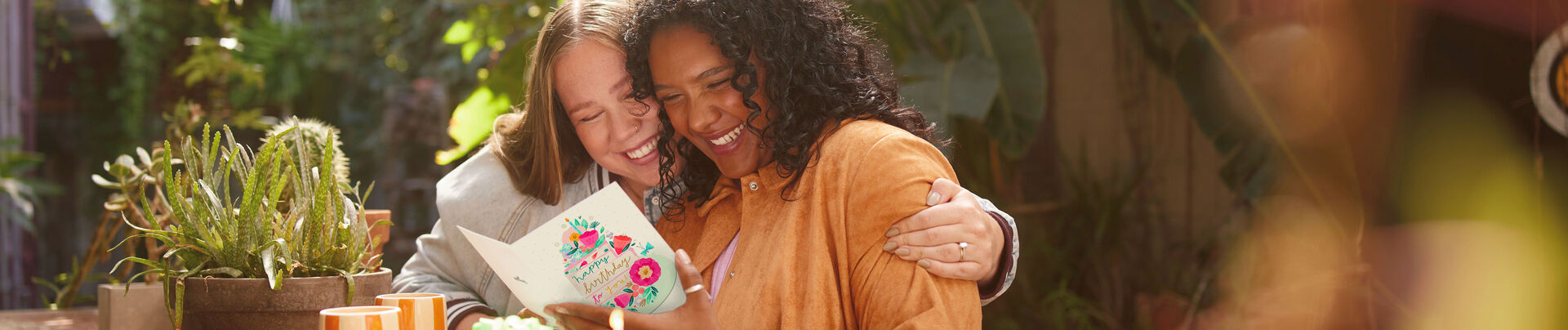 Two women hugging and smiling at a birthday card.