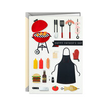 Card with papercut items used in grilling and “Happy Father’s Day” on a black ribbon