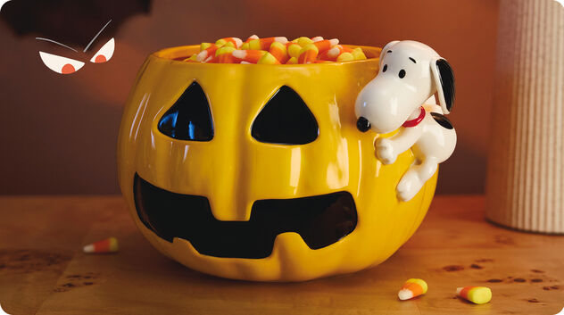 Pumpkin-shaped candy bowl with Snoopy hanging on the edge. 