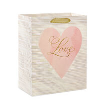 Gift bag with cursive "Love" over a pink heart and gold ribbon handle