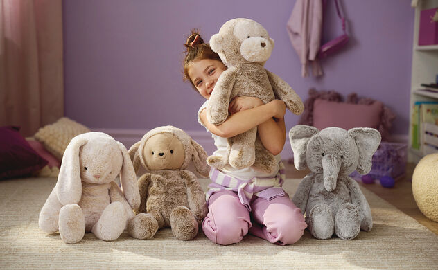  Girl in bedroom hugging a stuffed animal surrounded by 3 more stuffed animals.