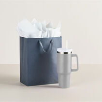 Large gift bag next to insulated travel mug with handle and straw.